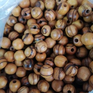May include: A close-up of a bag filled with round wooden beads. The beads are a light brown colour with dark brown stripes.