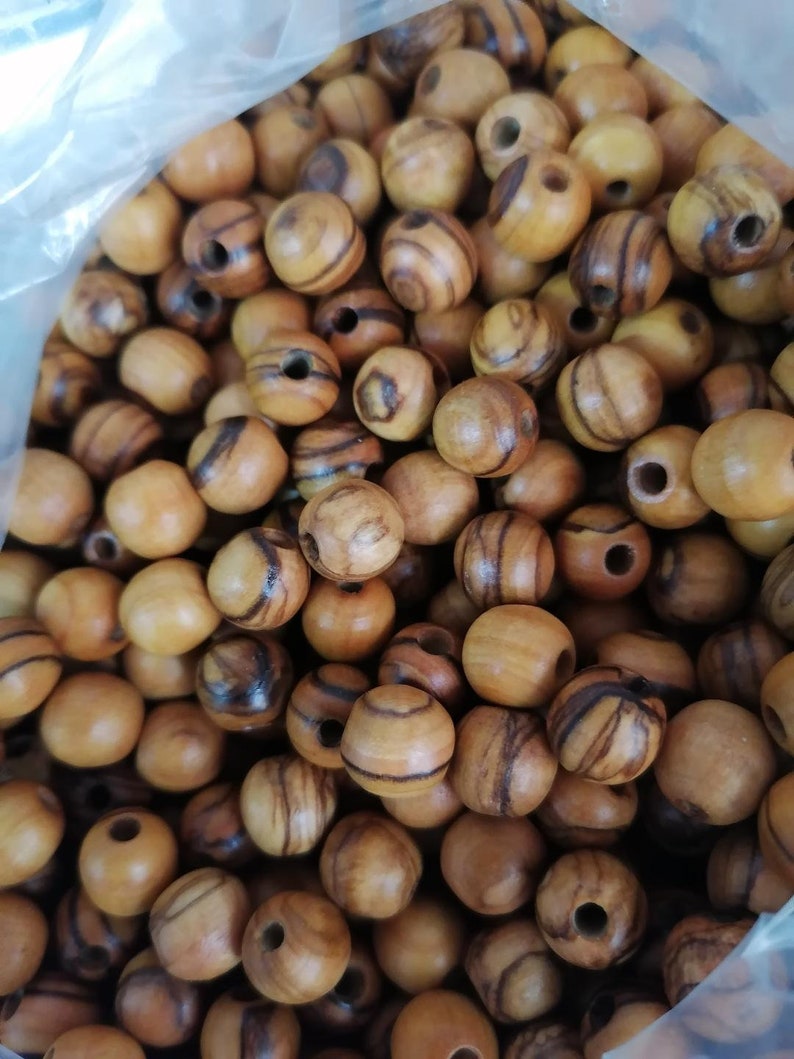May include: A close-up of a bag filled with round wooden beads. The beads are a light brown colour with dark brown stripes.