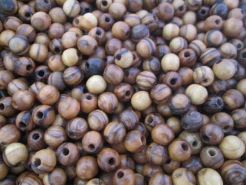 May include: A close-up of a pile of brown and black wooden beads with a hole in the center of each bead. The beads are round and have a natural wood grain pattern.