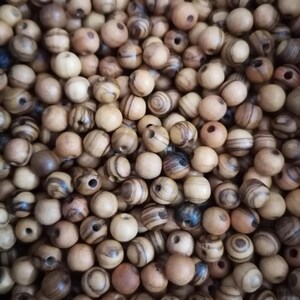 May include: A close-up image of a pile of wooden beads. The beads are round and have a natural wood colour with brown and black stripes. The beads are all about the same size and are perfect for making jewellery or other crafts.