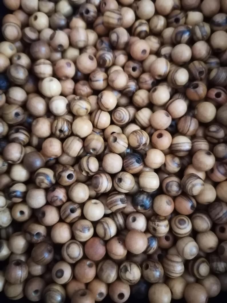 May include: A close-up image of a pile of wooden beads. The beads are round and have a natural wood colour with brown and black stripes. The beads are all about the same size and are perfect for making jewellery or other crafts.