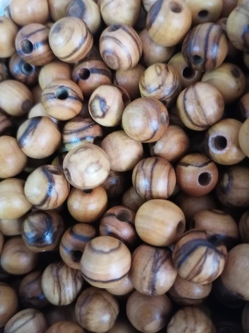 May include: A close-up of a pile of round wooden beads with dark brown stripes. The beads have a natural wood finish and are ideal for crafting.