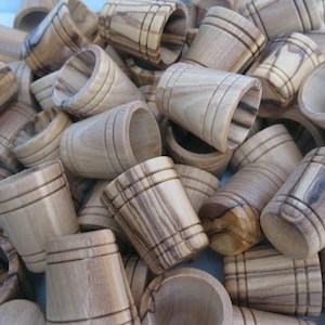 May include: A collection of small, light brown wooden cups with a cylindrical shape. Each cup has a slightly flared opening and is adorned with horizontal grooves. The cups are made of wood with a visible grain pattern.