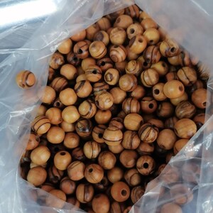 May include: A plastic bag filled with a large quantity of round wooden beads. The beads are a light brown colour with dark brown stripes.