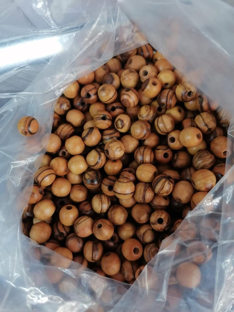 May include: A plastic bag filled with a large quantity of round wooden beads. The beads are a light brown colour with dark brown stripes.