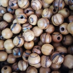 May include: A close-up of a pile of round wooden beads with brown and black stripes. The beads have a natural wood finish and are ideal for crafting.