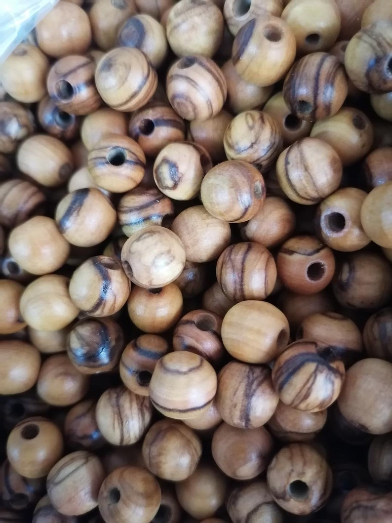 May include: A close-up of a pile of round wooden beads with brown and black stripes. The beads have a natural wood finish and are ideal for crafting.