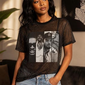 May include: A black short-sleeved t-shirt made of a sheer, glittery mesh fabric. The front features a rectangular graphic print divided into four vertical panels, each displaying a black and white portrait of a different person with distinct facial features.