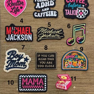 May include: A collection of eleven embroidered patches featuring various designs including a pink heart with text, text-based slogans, a musical note, a record player, and colorful summer-themed graphics with text like 'Realtor Life' and 'MAMA'.