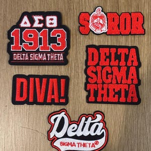 May include: A collection of embroidered patches with red and white text on a black background. The patches include the text "Patch Pack #1", "1913", "Delta Sigma Theta", "DIVA!", and "SOROR".