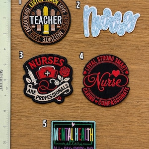 May include: Five embroidered patches next to a ruler showing inches. Patch 1 is a round black teacher badge. Patch 2 is light blue script text reading Nurse. Patch 3 is a black shield shape with medical icons. Patch 4 is a round black badge. Patch 5 is a rectangular Mental Health Matters patch.
