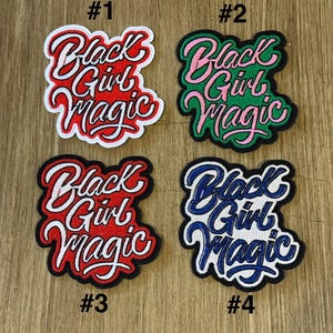 May include: Four embroidered patches with the phrase "Black Girl Magic" in a stylized script. Each patch has a different color scheme: red and white, pink and green, red and white, and blue and white. Numbers 1-4 are printed on the patches.