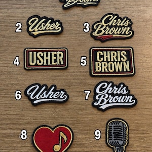 May include: A collection of nine embroidered patches featuring various designs. Items 1, 2, 3, 4, 5, 6, and 7 display the names Usher or Chris Brown in different fonts and colors. Item 8 is a red heart with a gold musical note, and item 9 is a microphone.