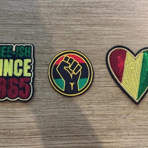 May include: Three embroidered patches featuring sequins. The first is a rectangular patch with the text "FREE-ISH SINCE 1865" in green, yellow, and red. The second is a circular patch with a black raised fist. The third is a heart-shaped patch.