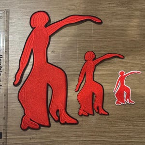 May include: Three red embroidered patches in the shape of a dancing figure, each in a different size. The largest patch measures approximately 6 inches in height, placed next to a clear plastic ruler for scale, showing the relative size of each.