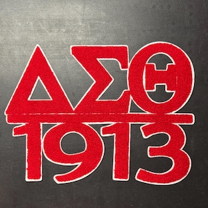 May include: A red chenille patch featuring the Greek letters Delta, Sigma, and Theta arranged horizontally above the number 1913. The design has a white border outlining the red textured letters and numbers, creating a bold, layered appearance.
