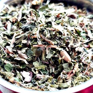 May include: A close-up of a bowl filled with a blend of dried herbs, including green leaves, brown stems, and white pieces. The herbs appear to be a mix of different types, creating a colorful and textured composition.
