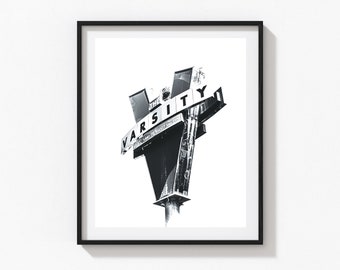 May include: Black and white photograph of a vintage sign for "The Varsity" restaurant. The sign is shaped like a V and has a weathered, distressed look.