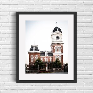 May include: A brick building with a clock tower and a white steeple. The building has a red brick facade and white trim. There are trees in front of the building.