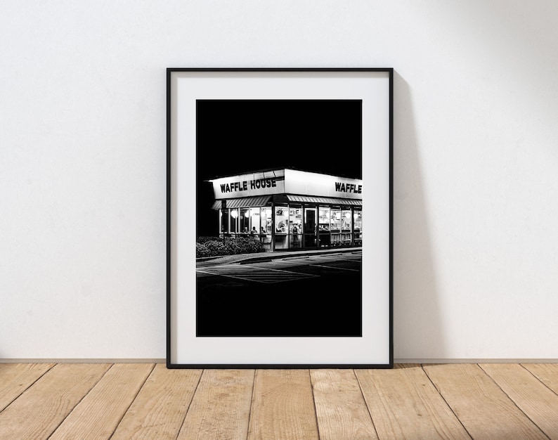 May include: A black and white photograph of a Waffle House restaurant at night. The sign above the entrance reads "Waffle House".
