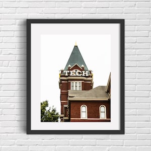 May include: A framed photograph of a brick building with a green roof and a gold spire. The building has a sign that reads "TECH" in white letters. The building is against a white background.