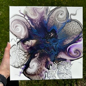 Puede incluir: Un lienzo cuadrado que presenta una pintura abstracta de vertido acr&iacute;lico con un n&uacute;cleo azul oscuro rodeado de patrones arremolinados de color morado, blanco y negro. El dise&ntilde;o incluye estructuras celulares intrincadas y efectos de pintura fluida.