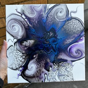 Puede incluir: Un lienzo cuadrado con una pintura abstracta de vertido acr&iacute;lico que presenta un n&uacute;cleo azul profundo que irradia hacia afuera en patrones de remolinos de color p&uacute;rpura, blanco y negro. El dise&ntilde;o incluye estructuras celulares y texturas fluidas.