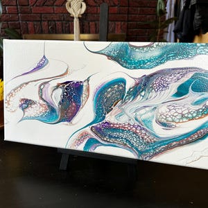 K&ouml;nnte beinhalten: Ein rechteckiges Leinwandgem&auml;lde mit einem abstrakten, fl&uuml;ssigen Acryl-Guss-Design. Das Kunstwerk zeigt wirbelnde Muster in T&uuml;rkis, Dunkelblau, Violett und Wei&szlig;, die durch komplexe zellenartige Strukturen und organische, flie&szlig;ende Linien gepr&auml;gt sind.