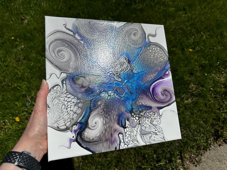Puede incluir: Un lienzo cuadrado con una pintura abstracta de vertido acr&iacute;lico sobre fondo blanco. El dise&ntilde;o muestra patrones de remolinos en plata met&aacute;lica, azul intenso y morado, con estructuras celulares intrincadas y formas org&aacute;nicas fluidas.