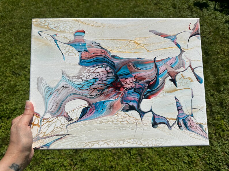 May include: Abstract acrylic pour painting on canvas. The artwork features a cream-colored background with flowing patterns in shades of blue, red, gold, and gray. The fluid art style creates a unique and textured visual effect.
