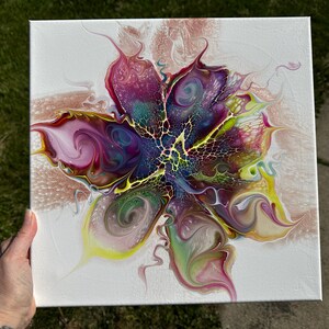 Pu&ograve; includere: Una tela quadrata che presenta un dipinto acrilico astratto con un design centrale simile a un fiore. La composizione mostra vortici vibranti di magenta, viola intenso, giallo brillante e verde acqua, accentuati da intricati motivi cellulari bianchi e dorati.
