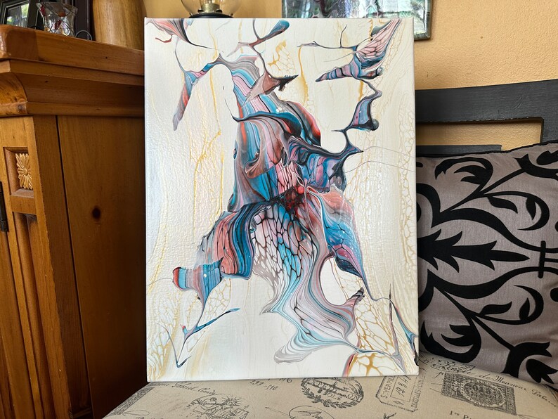May include: Abstract acrylic painting on canvas. The artwork features a cream-colored background with flowing patterns in shades of blue, pink, and black. The design has a fluid, organic appearance with a cracked, textured effect.