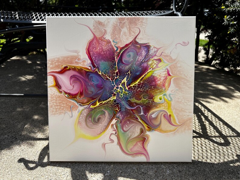 Pu&ograve; includere: Un dipinto su tela quadrata che presenta un design astratto a colata acrilica fluida. Il centro mostra un vivace motivo floreale multicolore con sfumature vorticose di magenta, viola, giallo e verde acqua, accentuato da una distinta struttura cellulare nera.