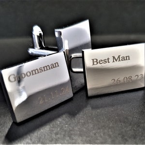 May include: Silver rectangular cufflinks, one marked "Groomsman" and "21.11.24", the other "Best Man" and "26.08.23". The cufflinks are presented in a dark box. A classic accessory for a wedding.
