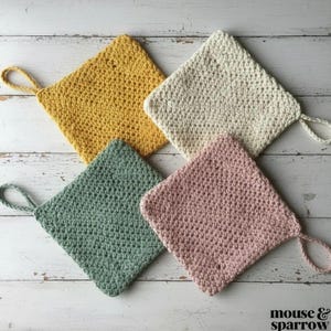 May include: Four square crochet pot holders in mustard yellow, cream, sage green, and dusty pink. Each pot holder features a textured stitch pattern and a small braided loop attached to one corner for hanging. The text mouse and sparrow is visible.