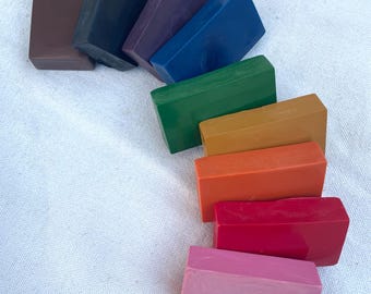 May include: A collection of rectangular, solid-colored wax blocks in various shades. Colors include brown, black, purple, blue, green, orange, red, and pink. The blocks are arranged in a diagonal line against a white background.