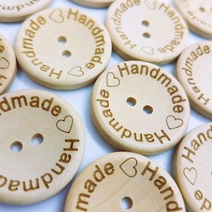 May include: A close-up of several wooden buttons with the word "Handmade" and a heart symbol engraved on them. The buttons are light brown and have two holes each.