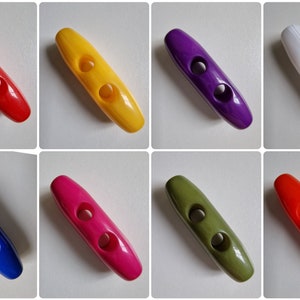 May include: A collection of eight oblong, two-holed buttons in various colors: red, yellow, purple, white, blue, pink, olive green, and orange. The buttons are smooth and glossy, suitable for sewing projects or crafts.
