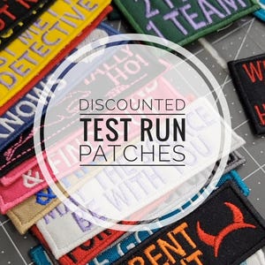 May include: A collection of embroidered patches in various colors, featuring phrases like "TEST RUN PATCHES" and "4 PAWS 2 FEET 1 TEAM." The patches have different colored borders and text, including yellow, green, and black.