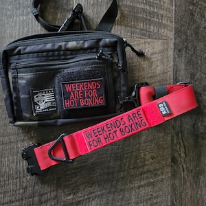 Puede incluir: Un cinturón negro y de camuflaje y un collar rojo para perros. El cinturón tiene un parche que dice "WEEKENDS ARE FOR HOT BOXING". El collar para perros también tiene el mismo texto en rojo.