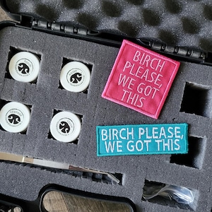 May include: A black carrying case with grey foam inserts containing four small white circular containers labeled birch, anise, cypress, and clove. Included are a pink square patch and a teal rectangular patch, both embroidered with the text BIRCH PLEASE, WE GOT THIS, and a pair of silver metal tweezers.