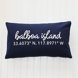 May include: Navy blue throw pillow with white text that reads "balboa island 33.6073° N, 117.8971° W"
