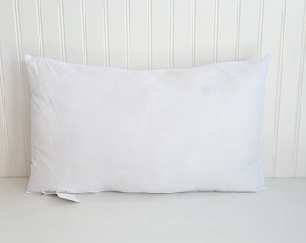 May include: A white pillow with a white tag attached to the bottom corner.