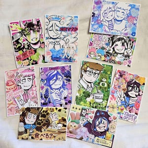 Może przedstawiać: Kolekcja kolorowych, ilustrowanych kart artystycznych z postaciami w stylu anime i różnymi elementami dekoracyjnymi. Każda karta prezentuje unikalne wzory, w tym tekst, kwiatowe akcenty i postacie z kreskówek.