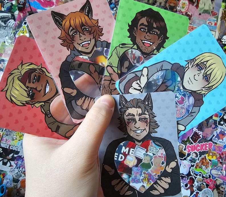 Może przedstawiać: Dłoń trzymająca pięć kart z grafikami postaci. Każda karta przedstawia inną postać w stylu anime z wilczymi uszami. Karty mają tła z r&oacute;żowych serc, zieleni i błękitu. Centralna karta ma serce z napisem "ME ED" i kolorowymi naklejkami z misiami.