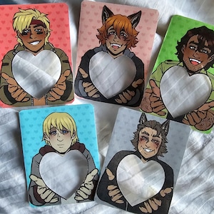 Puede incluir: Cinco tarjetas ilustradas con personajes de estilo anime sosteniendo recortes en forma de corazón. Cada tarjeta tiene un color de fondo diferente: rojo, rosa, verde, azul y gris. Los personajes tienen varios tonos de piel y colores de cabello.