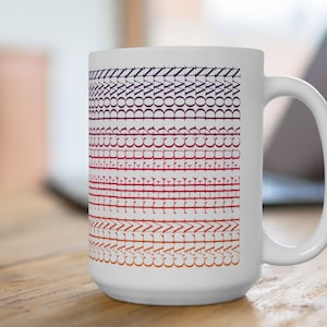 May include: White ceramic mug with a repeating pattern of stylized text in a gradient of colors from dark purple to orange. The mug has a large handle and is sitting on a wooden surface.