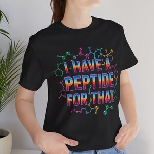 May include: Black t-shirt with the text "I HAVE A PEPTIDE FOR THAT" in a rainbow gradient. The design includes a colorful molecular structure around the text. The shirt is made of a soft material.