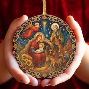Puede incluir: Adorno navideño redondo con una escena de la Natividad con María, José y el niño Jesús. El adorno tiene un borde dorado y un lazo dorado para colgar. El fondo es azul oscuro con una estrella y un ángel.