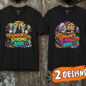 May include: Two black t-shirts featuring a graphic print with the text SPOOKY STRONG 2026. The design includes skeletons lifting rainbow-colored barbells, pumpkins, ghosts, and fitness equipment in vibrant colors against a dark background.